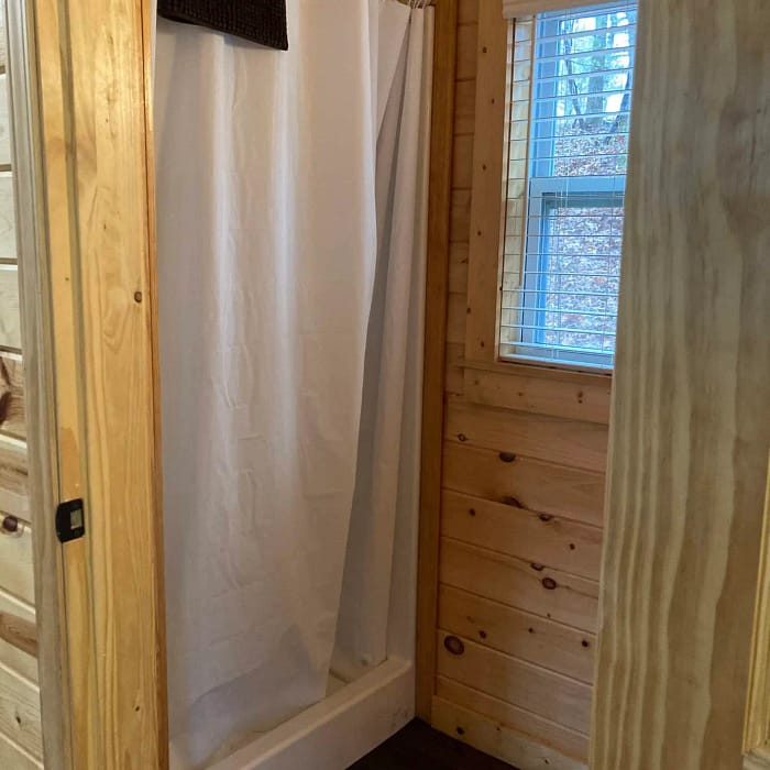 A wooden bathroom interior with a white shower curtain and a window providing natural light.