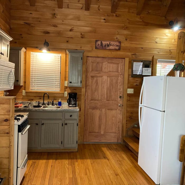 A cozy wooden cabin kitchen with basic appliances and a "welcome" sign above the door.