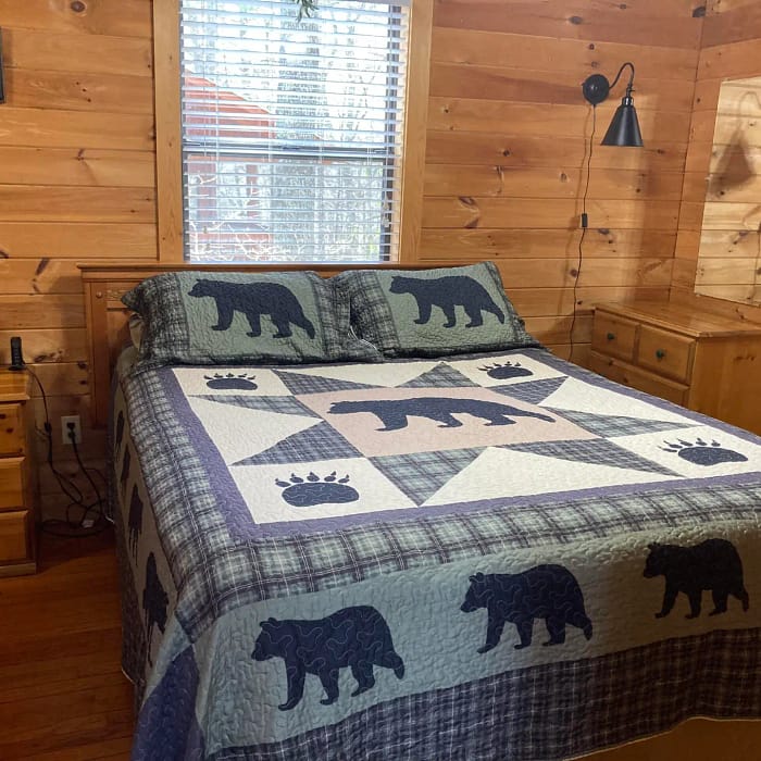 A rustic bedroom with a bear-themed quilt on a bed and wooden walls.