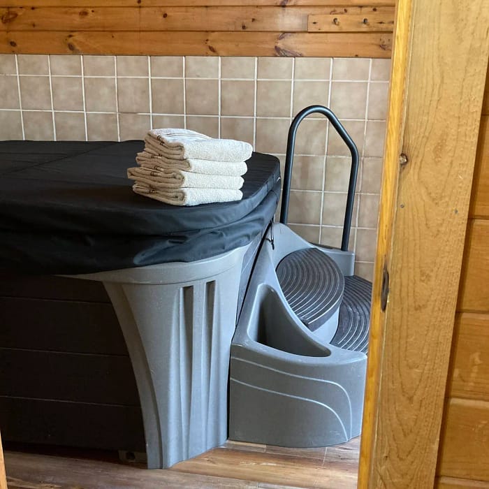 A stack of towels on top of a hot tub cover next to a plastic step stool and bathing accessories.