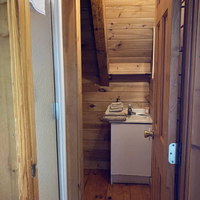 A small wooden bathroom with a sink and towels, featuring a wooden door ajar to the left.