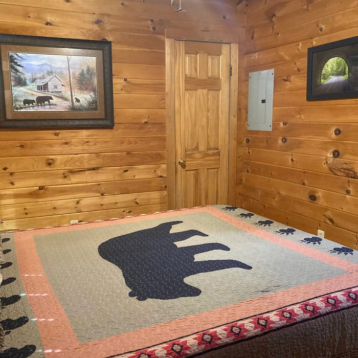 A rustic wooden cabin interior with a bear-themed quilt on the bed and wildlife art on the walls.