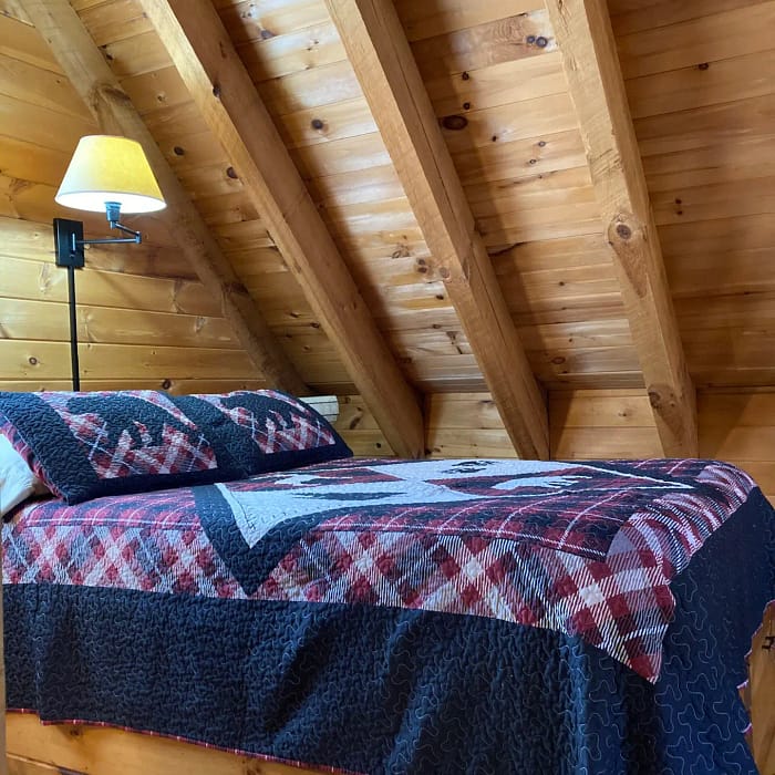 A cozy attic bedroom with wooden walls and a plaid-covered bed.