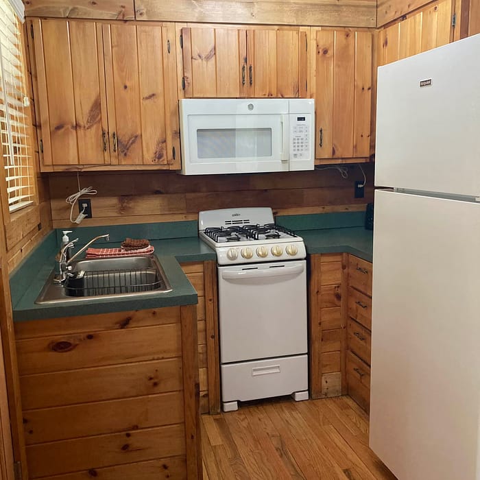 A compact wooden kitchen with modern appliances including a microwave, stovetop, sink, and refrigerator.