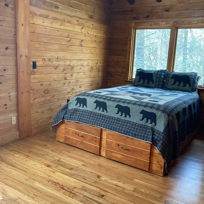 A wooden cabin bedroom with a bed featuring a bear-patterned blanket.