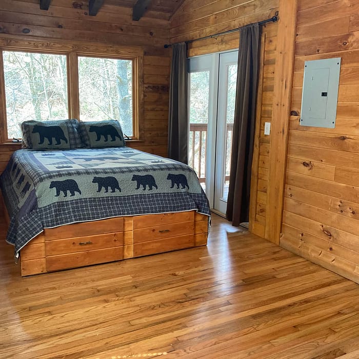 A rustic wooden bedroom with a bear-themed bedspread and sliding door access to the outside.