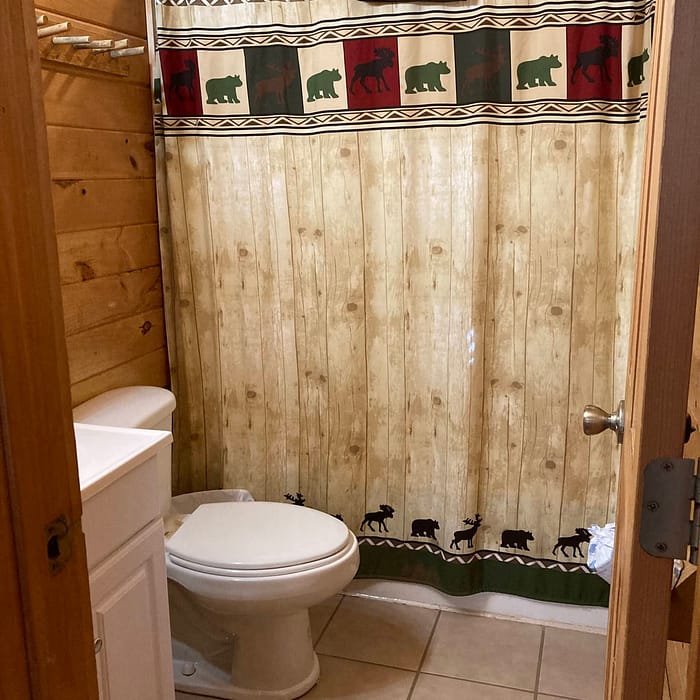 A rustic bathroom with a wooden wall theme and a shower curtain featuring bear and moose silhouettes.