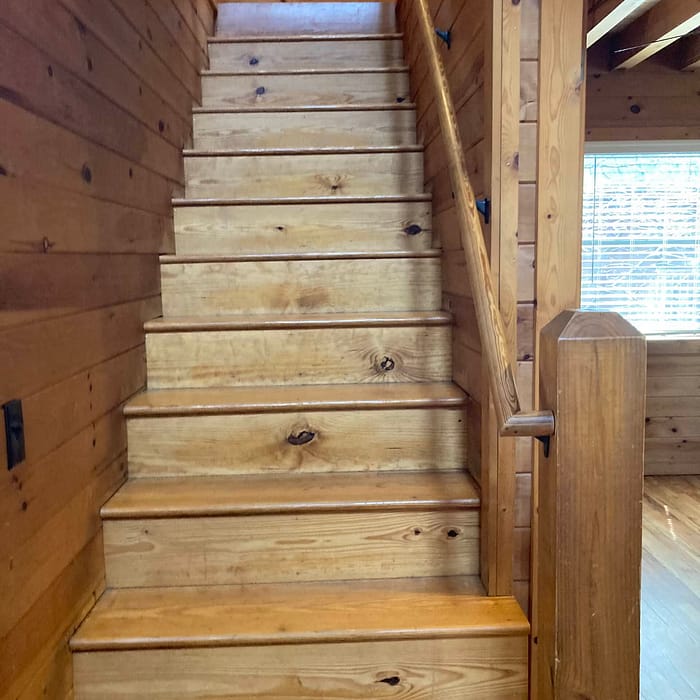 Wooden staircase in a cabin-like interior with natural light coming from a window.