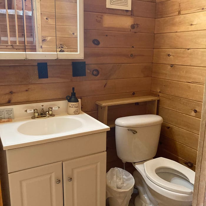 A cozy wooden-paneled bathroom with a sink, toilet, and mirrored medicine cabinet.