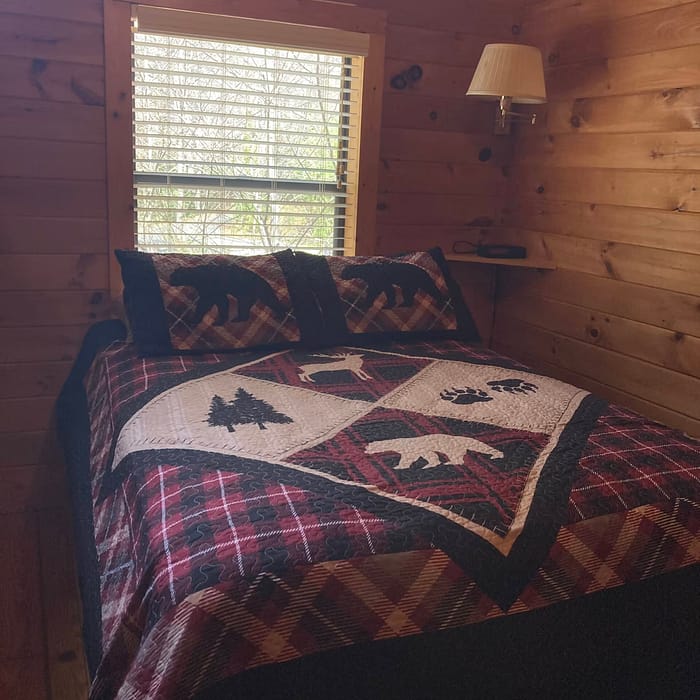 A cozy cabin bedroom featuring a bed with a quilted wildlife-themed bedspread and a window with blinds.