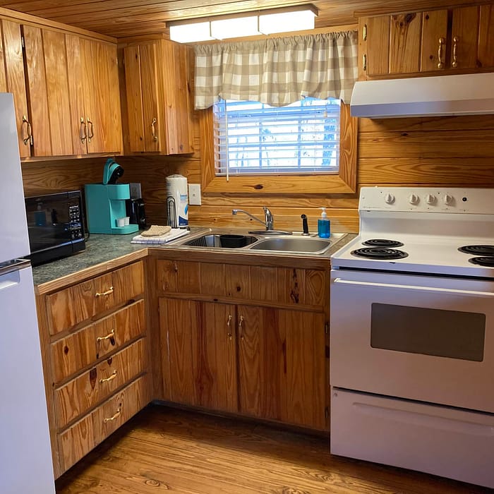 A small, wood-paneled kitchen with white appliances and a window above the sink.