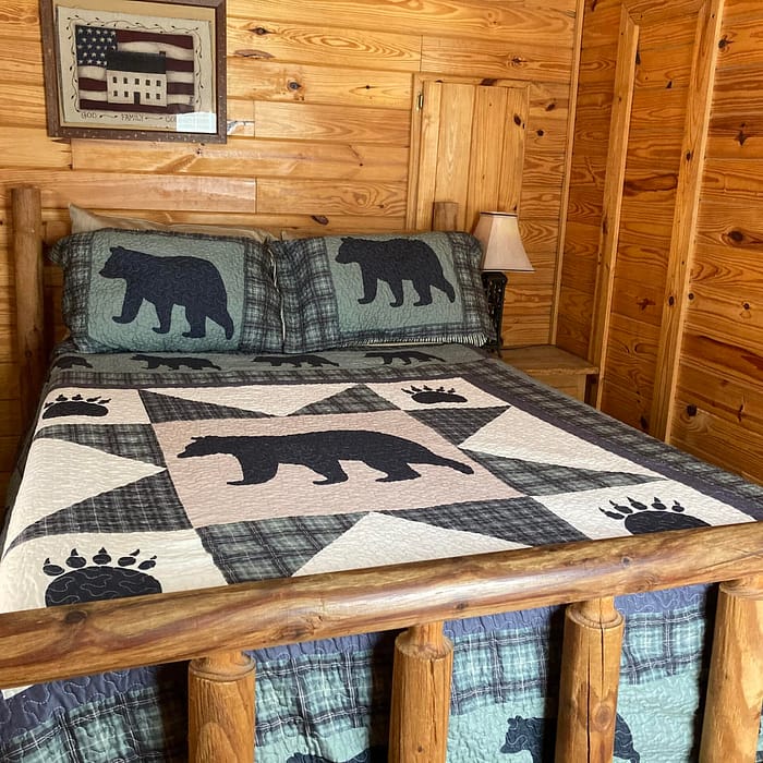 A rustic cabin bedroom featuring a bed with a bear and paw print quilt pattern.