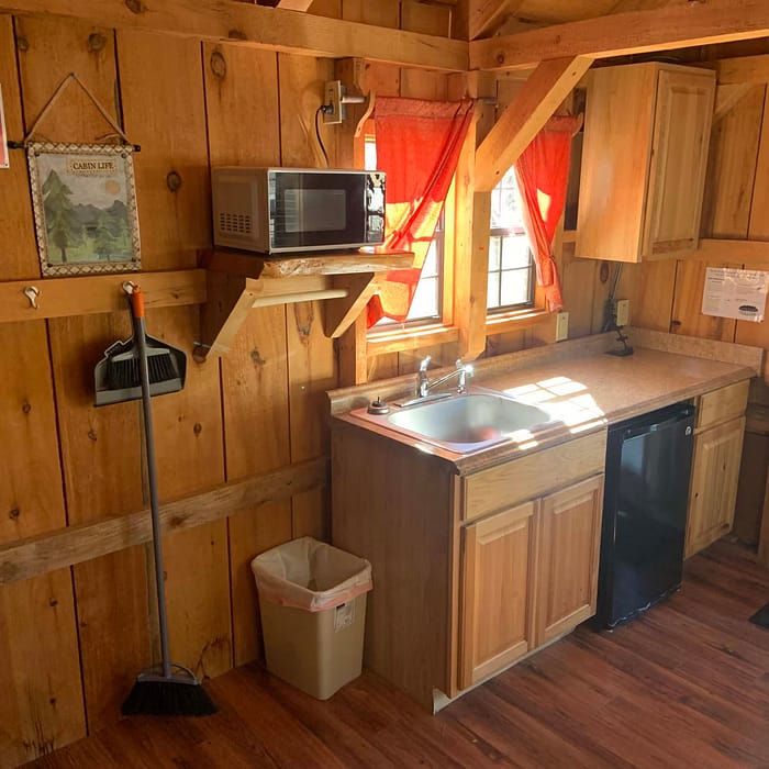 A cozy wooden cabin kitchenette with basic appliances and a red curtain.