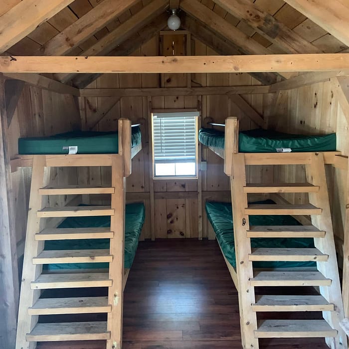 Wooden cabin interior with two symmetrical loft beds and ladders.