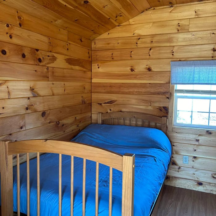 A simple wooden cabin bedroom with a neatly made bed and natural light from a window.