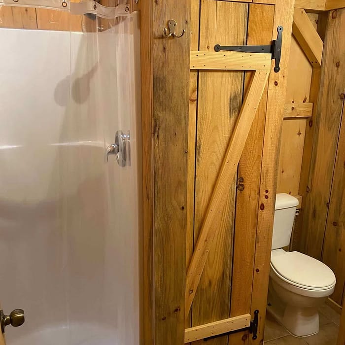 Wood-paneled bathroom with shower enclosure and toilet, featuring a barn-style sliding door.