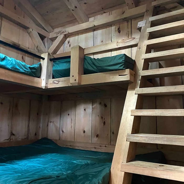 A wooden bunk bed with green bedding and stairs in a rustic cabin setting.