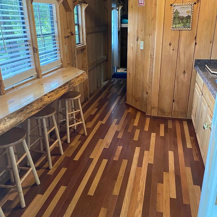 Interior of a cozy wooden cabin with a kitchenette and bar stools.