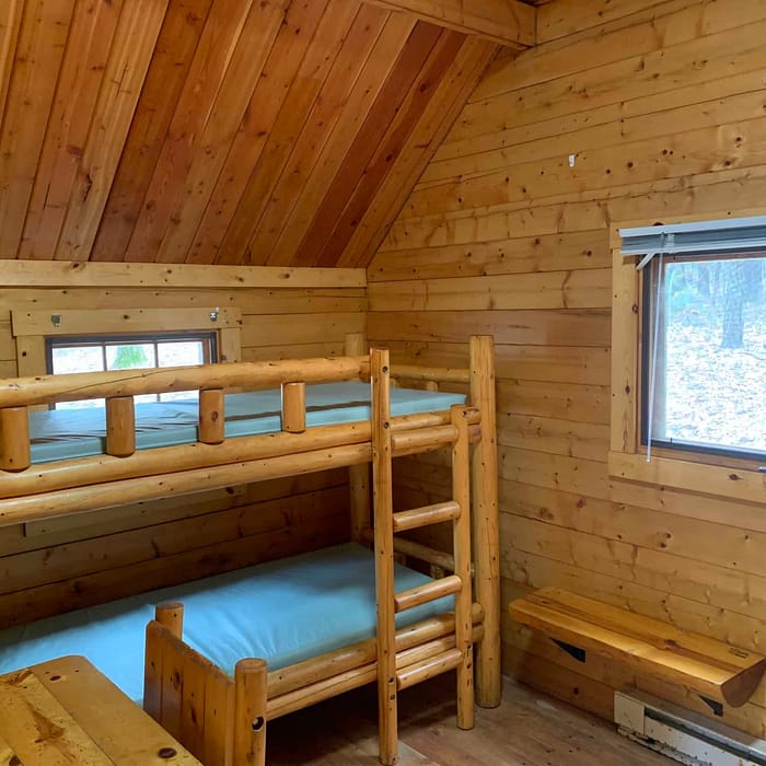 Cozy wooden cabin interior with bunk beds and a view of the forest through the window.
