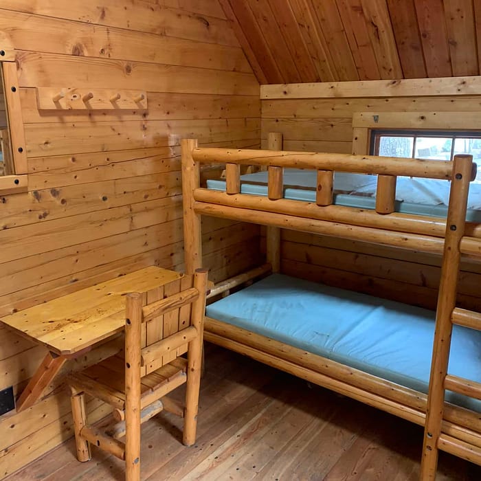 A rustic wooden bunk bed and desk in a cabin room with paneled walls.