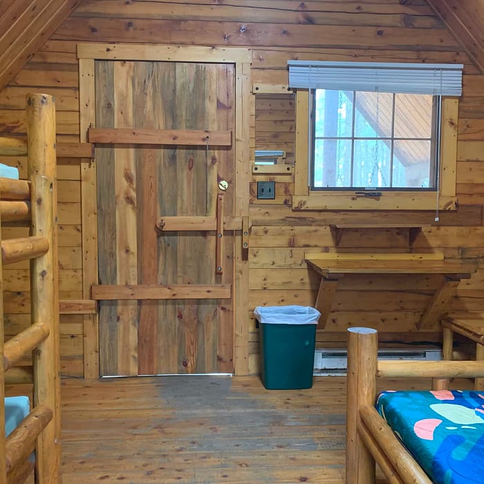 Rustic wooden cabin interior with bunk beds and a small desk under a window.