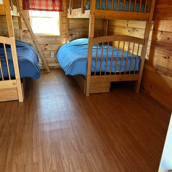 A small wooden cabin interior with two sets of bunk beds covered with blue bedding.