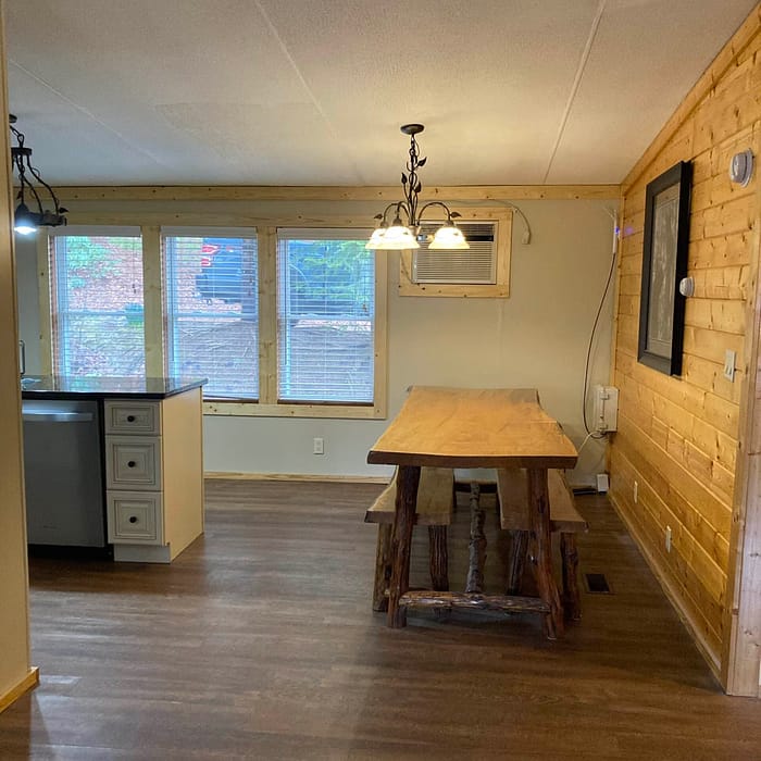 A cozy, well-lit dining space with a rustic wooden table, hardwood floors, and a kitchenette in the background.
