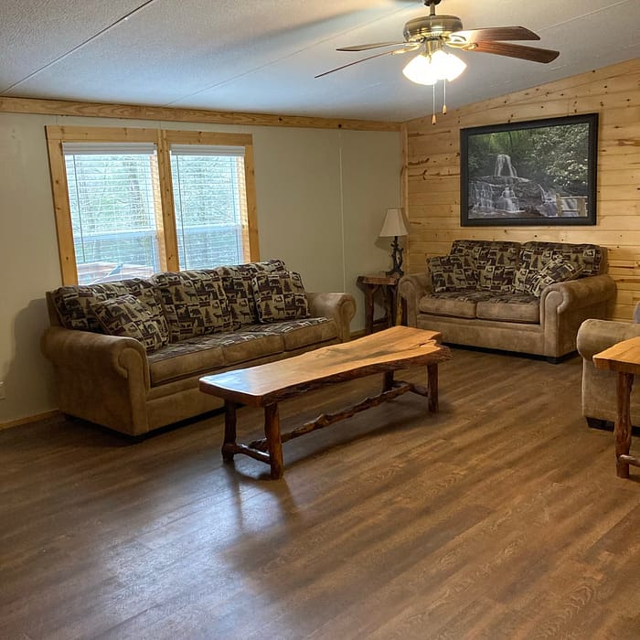 A cozy living room with wooden walls, a patterned sofa set, a wooden coffee table, and a television mounted on the wall.