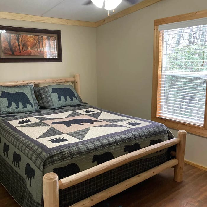 A cozy bedroom with a rustic wooden bed frame, quilted bear-patterned bedding, and a ceiling fan above.