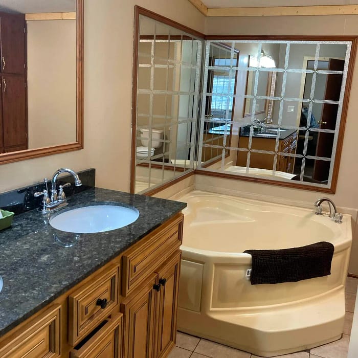 A bathroom interior featuring a large mirror, a bathtub with steps, a sink with wooden cabinets, and tiled flooring.