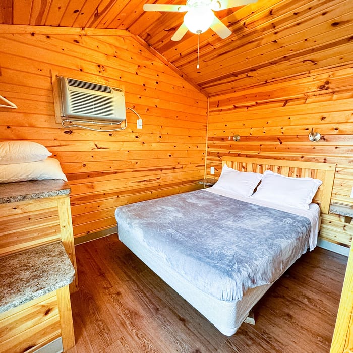 Wood-paneled bedroom with a double bed and a bunk bed under a running ceiling fan.