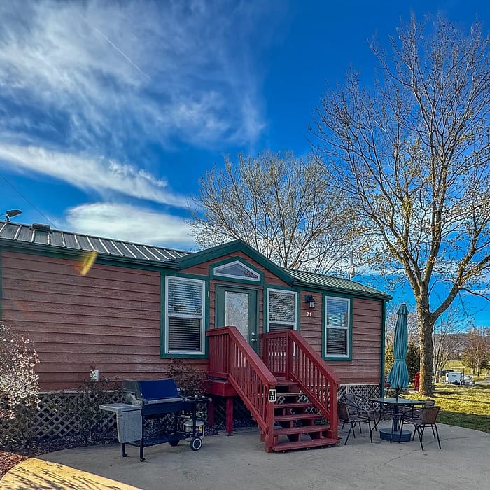 A small, cozy wooden cabin with a red staircase and outdoor furniture set under a clear blue sky.