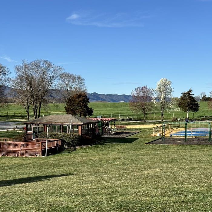A serene park setting with a playground, a wooden deck area, and a backdrop of rolling hills under a clear blue sky.