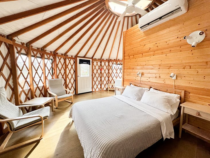 Cozy wooden yurt interior with a double bed, chairs, and modern amenities.