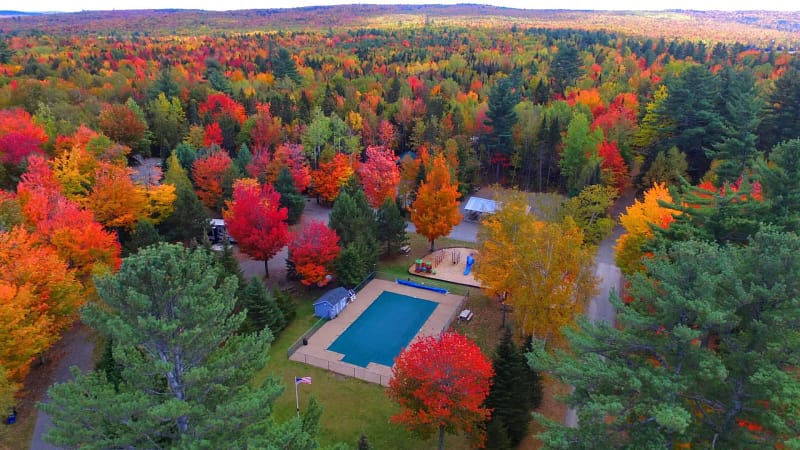 Experience a stunning aerial view of a pool nestled among fall colored trees at Spacious Skies Campgrounds.