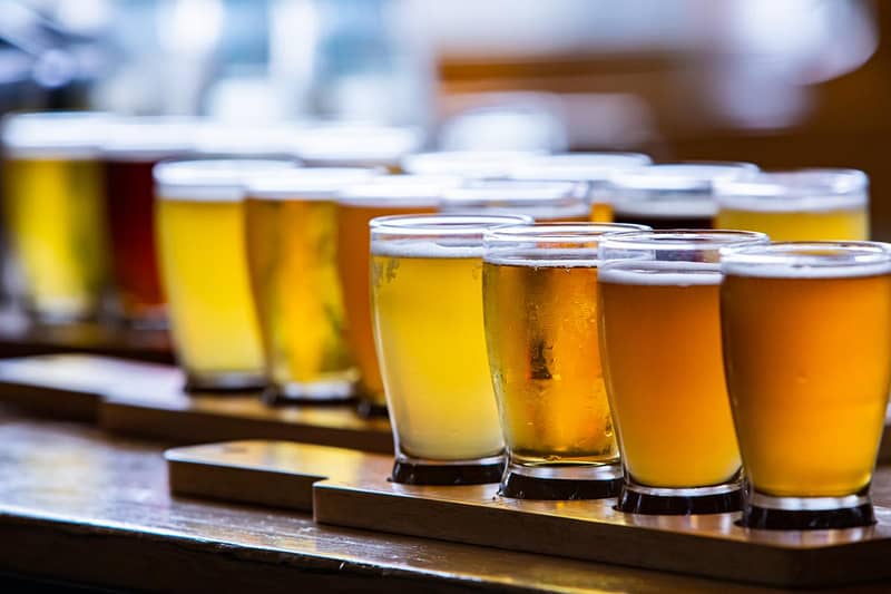 A variety of beer glasses filled with different types and colors of beer are arranged in rows on a wooden surface.