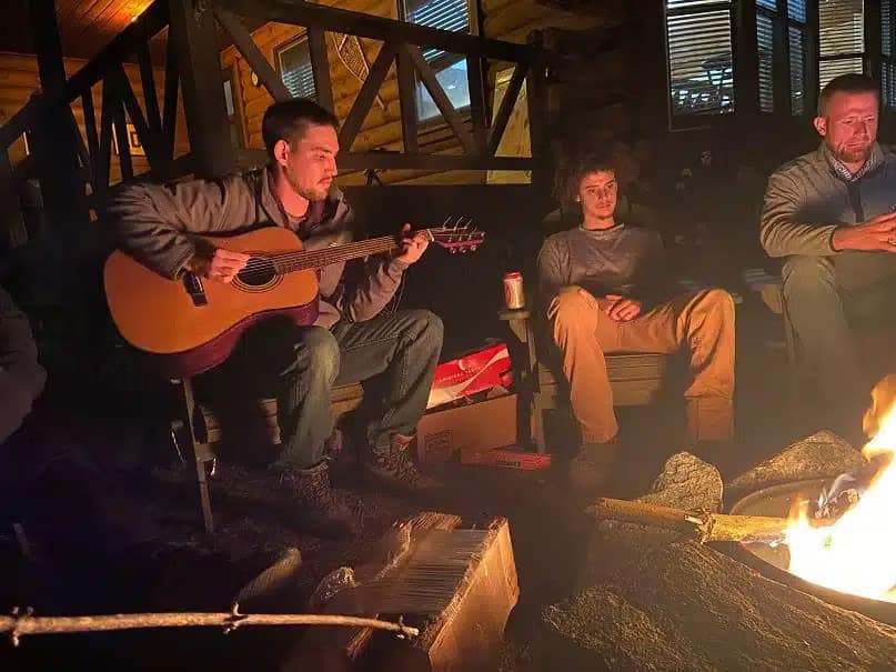 A group of people gathered around a campfire with guitars under the spacious skies.