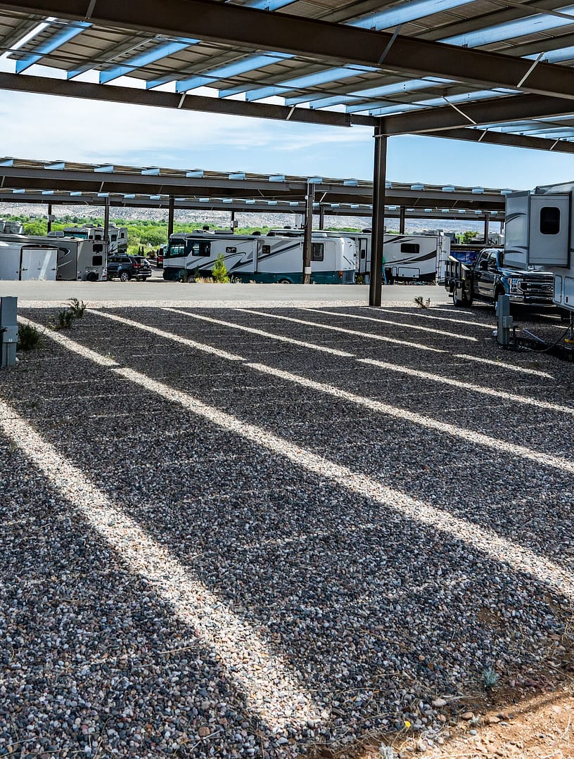 Covered parking area with gravel ground, metal roof, and several parked RVs and trailers visible in the background under the structure.