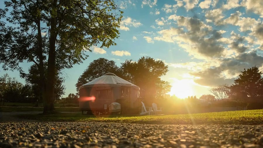 A yurt on a gravel road with the sun setting behind it.