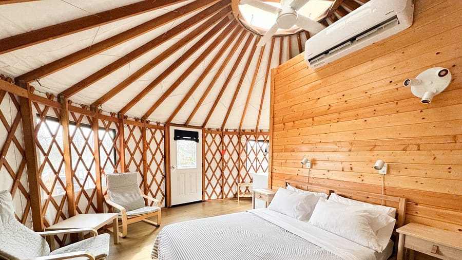 Cozy wooden yurt interior with a double bed, chairs, and modern amenities.