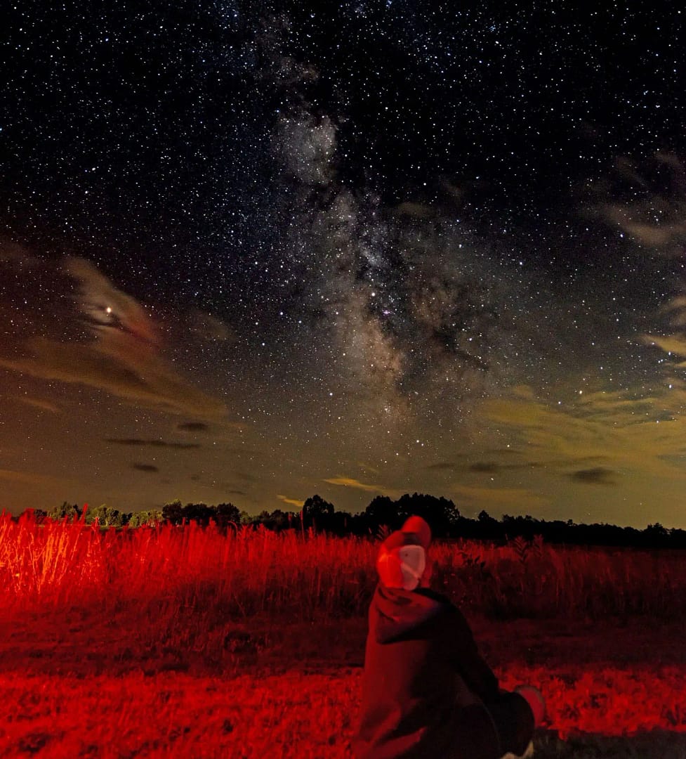 A person sitting in a field gazing up at the milky.